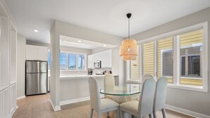 A modern kitchen with white cabinets, stainless steel appliances, and a glass dining table with chairs. - Completely Updated 2BR Condo–Cedars East #613 by RVA (Longboat Key)