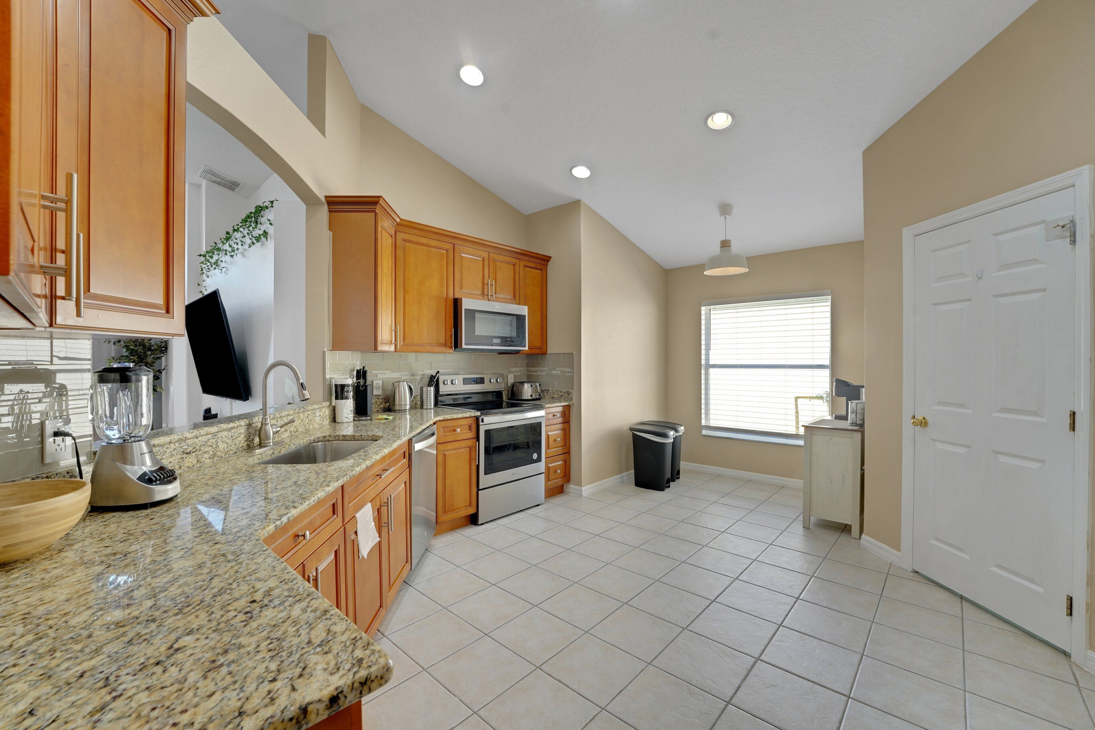 A kitchen with granite countertops, wooden cabinets, a microwave, stove, and a trash can.