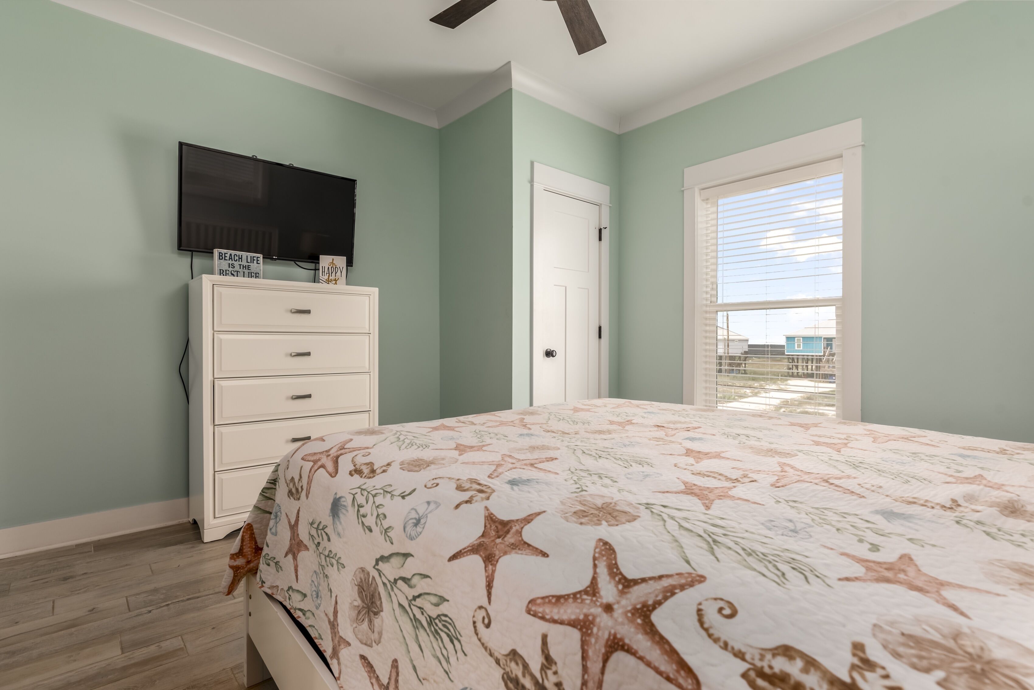 A bedroom with a bed, a dresser, a television, and a door leading to a balcony.