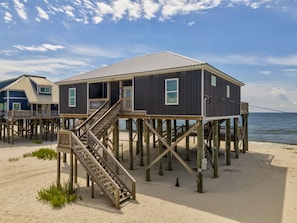 Une structure en bois située en bord de mer, avec un escalier menant à une terrasse, le tout entouré de sable et d’eau.