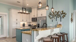A modern kitchen with white cabinets, a granite countertop, and a central island with stools. - Sea La Vie - 106 Velasco Ct 4 Bedroom Home (Dauphin Island)
