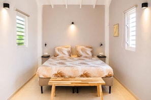 A bedroom with a bed, bedside tables, a bench, and a wall-mounted light fixture. - Bunitesa di bida Kas Iquana (Soto)