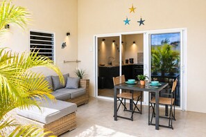 A modern living space with a sofa, dining table, chairs, and a kitchen area visible through a sliding door. - Bunitesa di bida Kas Iquana (Soto)