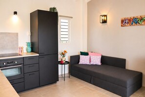 A compact living space with a kitchenette, a sofa with decorative pillows, and a wall-mounted artwork. - Bunitesa di bida Kas Iquana (Soto)