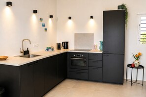A modern kitchen with black cabinets, a stainless steel sink, a built-in oven, and a black refrigerator. - Bunitesa di bida Kas Iquana (Soto)