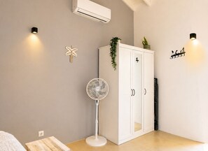 A room with a white wardrobe, a standing fan, and wall-mounted lights. - Bunitesa di bida Kas Iquana (Soto)