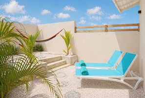 Un espace extérieur ensoleillé comprenant un fauteuil de relaxation, un hamac et un petit jardin avec des plantes.
