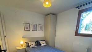 A bedroom with a bed, nightstands, a lamp, a fur rug, and a window with a view of trees. - T3 apartment 50 meters from the slopes - Heart of the resort. (Les Deux Alpes)
