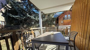 An outdoor patio with a table and chairs, a wooden deck, and a view of a building with a balcony. - T3 apartment 50 meters from the slopes - Heart of the resort. (Les Deux Alpes)