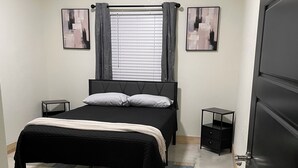 A bedroom with a bed, two bedside tables, a window with curtains, and two framed pictures on the wall. - Country Condo
 2-bedroom  with AC in Carl Junction (Carl Junction)