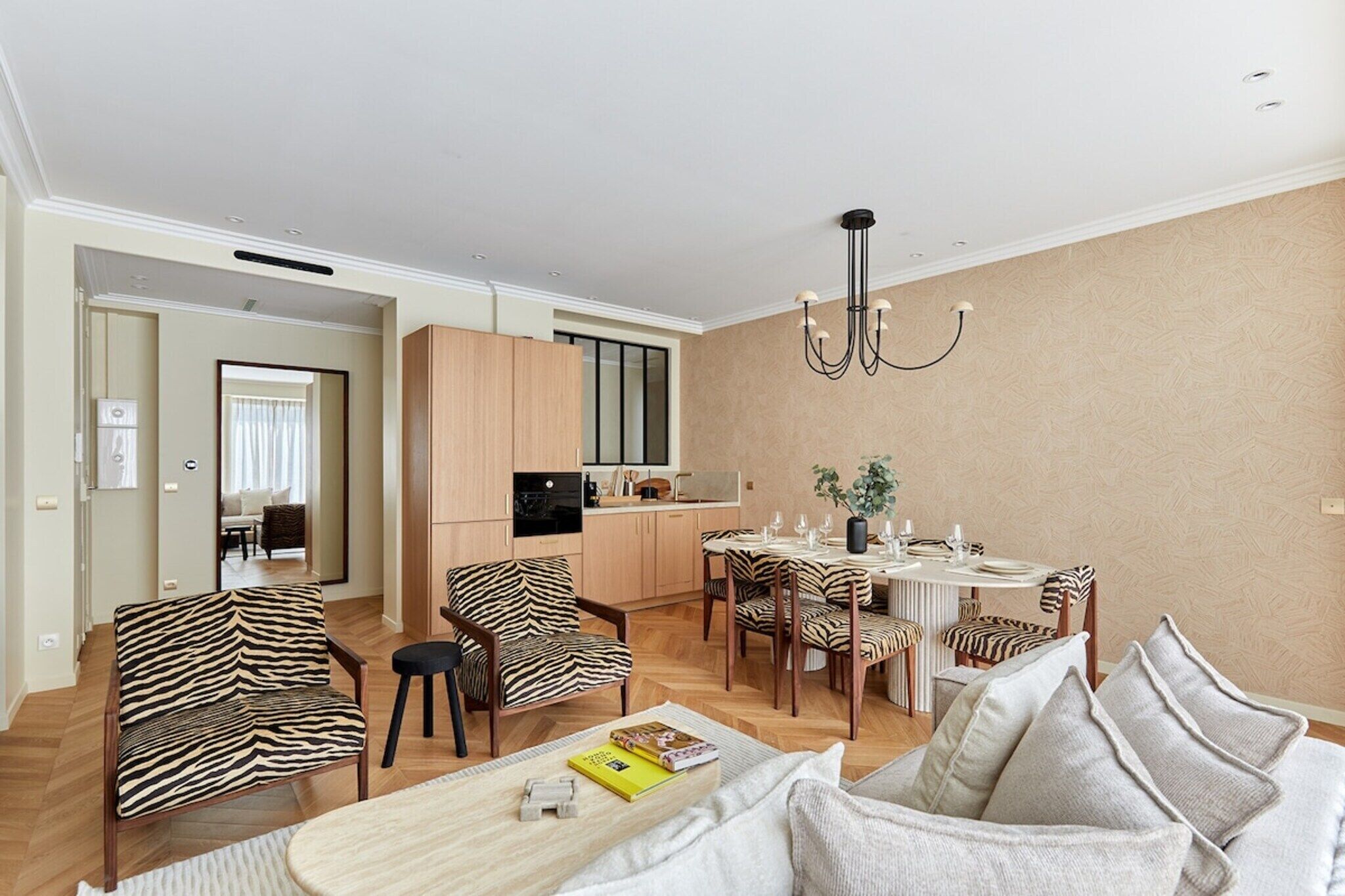 A modern living room with a zebra-patterned sofa, a dining table set for six, and a kitchen in the background.