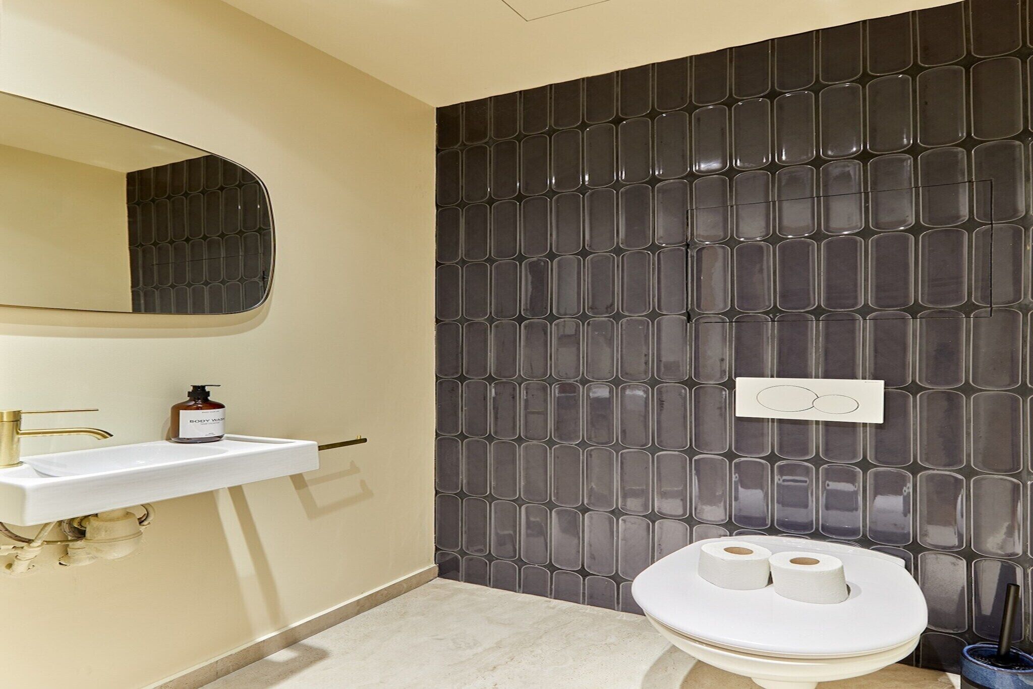 A bathroom with a white sink, a mirror, a toilet with two rolls of toilet paper, and a wall with a geometric tile pattern.
