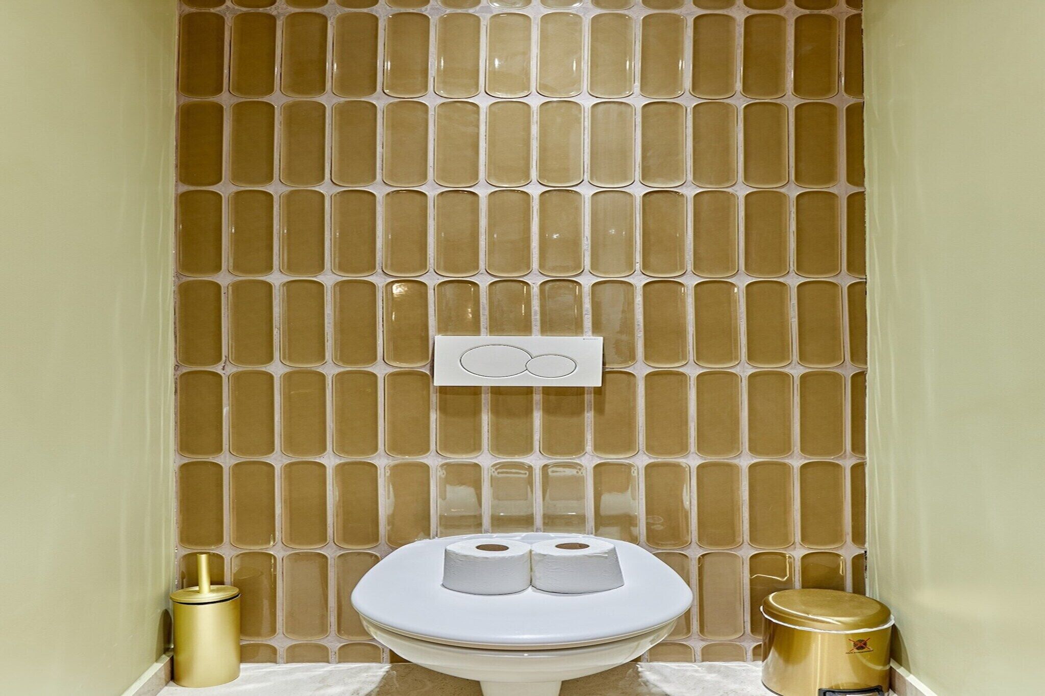 A bathroom with a toilet, two rolls of toilet paper, and two gold trash bins.