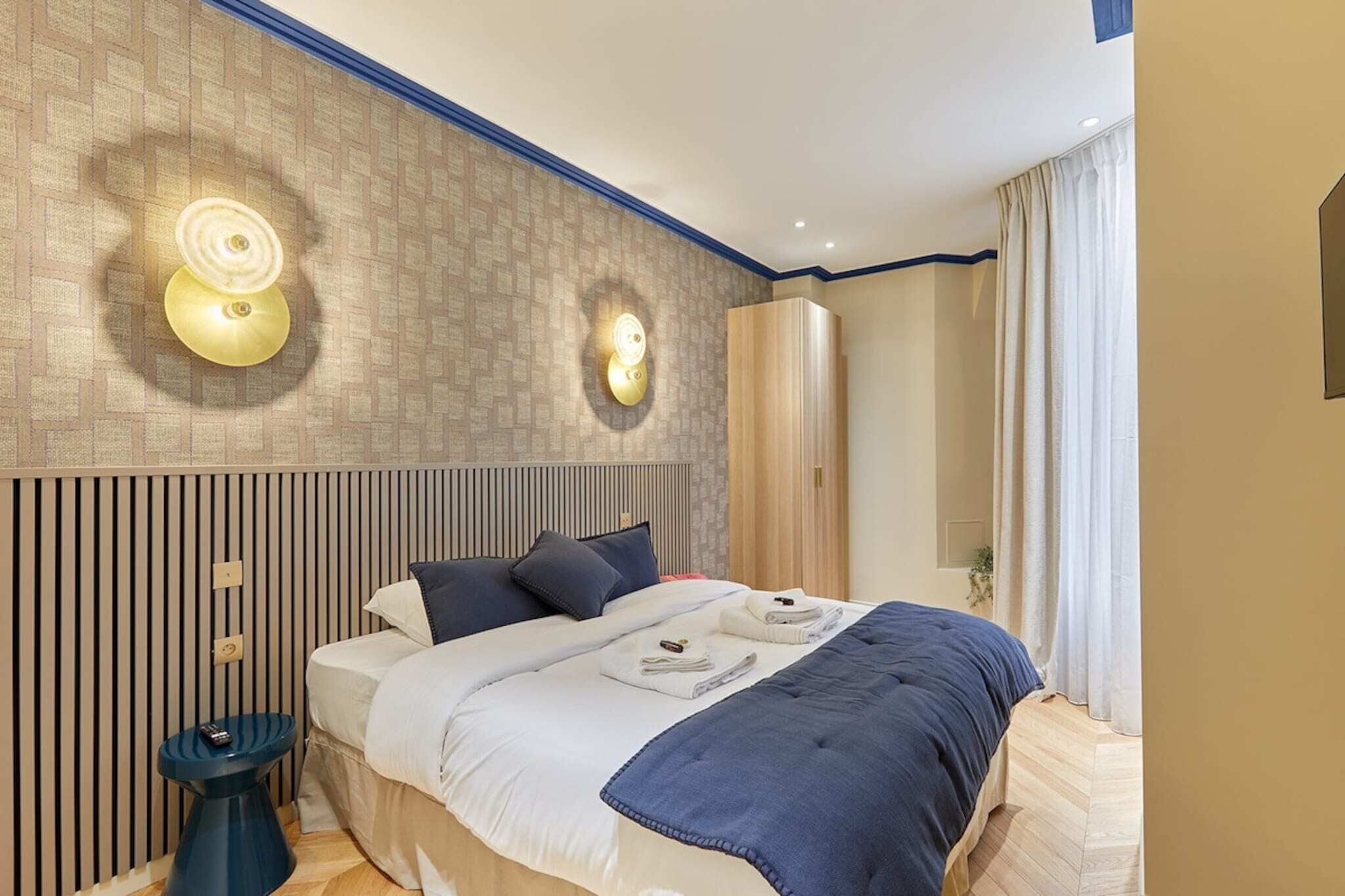 Een moderne hotelkamer met een groot bed, twee wandlampen, een nachtkastje en een raam met gordijnen.