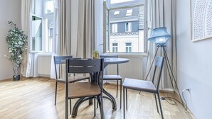Una habitación con una mesa redonda, sillas, una planta en maceta, una lámpara de pie y un ventanal con cortinas.