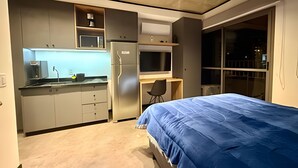 A compact bedroom with a bed, a small kitchenette, and a window. - Modern Studio at On Maracatins (São Paulo)