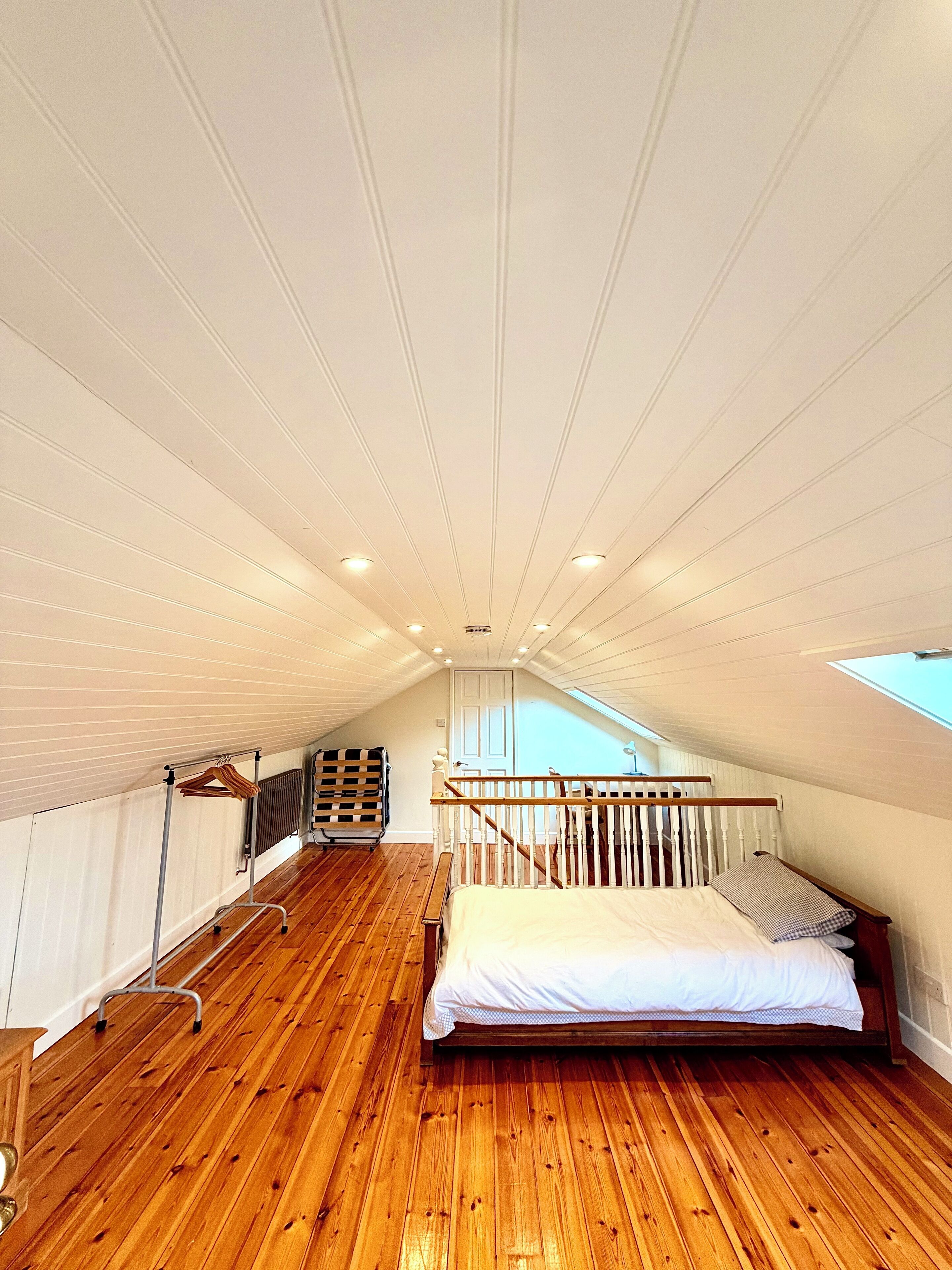 Une chambre avec un plancher en bois, un lit, un radiateur, un porte-vêtements et une lucarne.