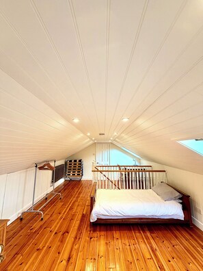 Une chambre avec un plancher en bois, un lit, un radiateur, un porte-vêtements et une lucarne.