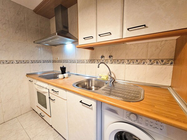 A compact kitchen with a built-in oven, a sink, and a washing machine. - Apartamentos Casa Boira 3000 (Biescas)