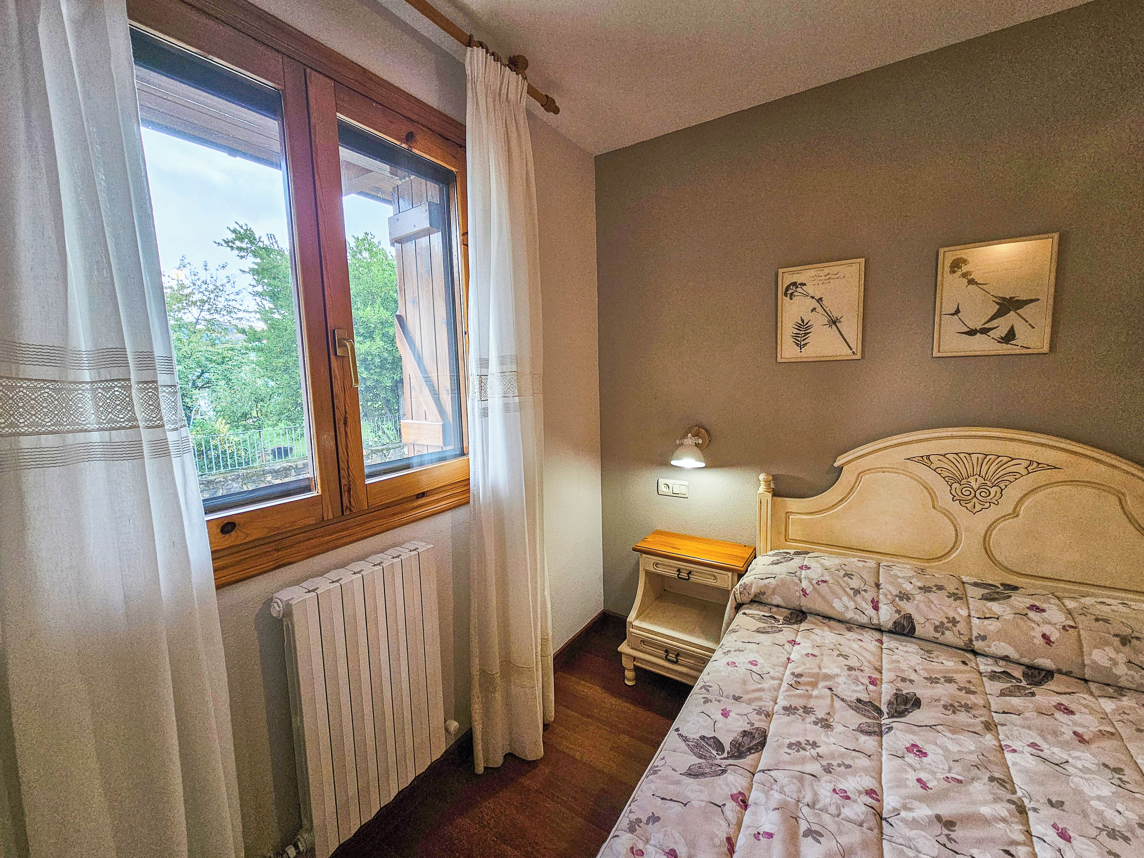 A bedroom with a wooden bed, a nightstand, a radiator, and a window with curtains.
