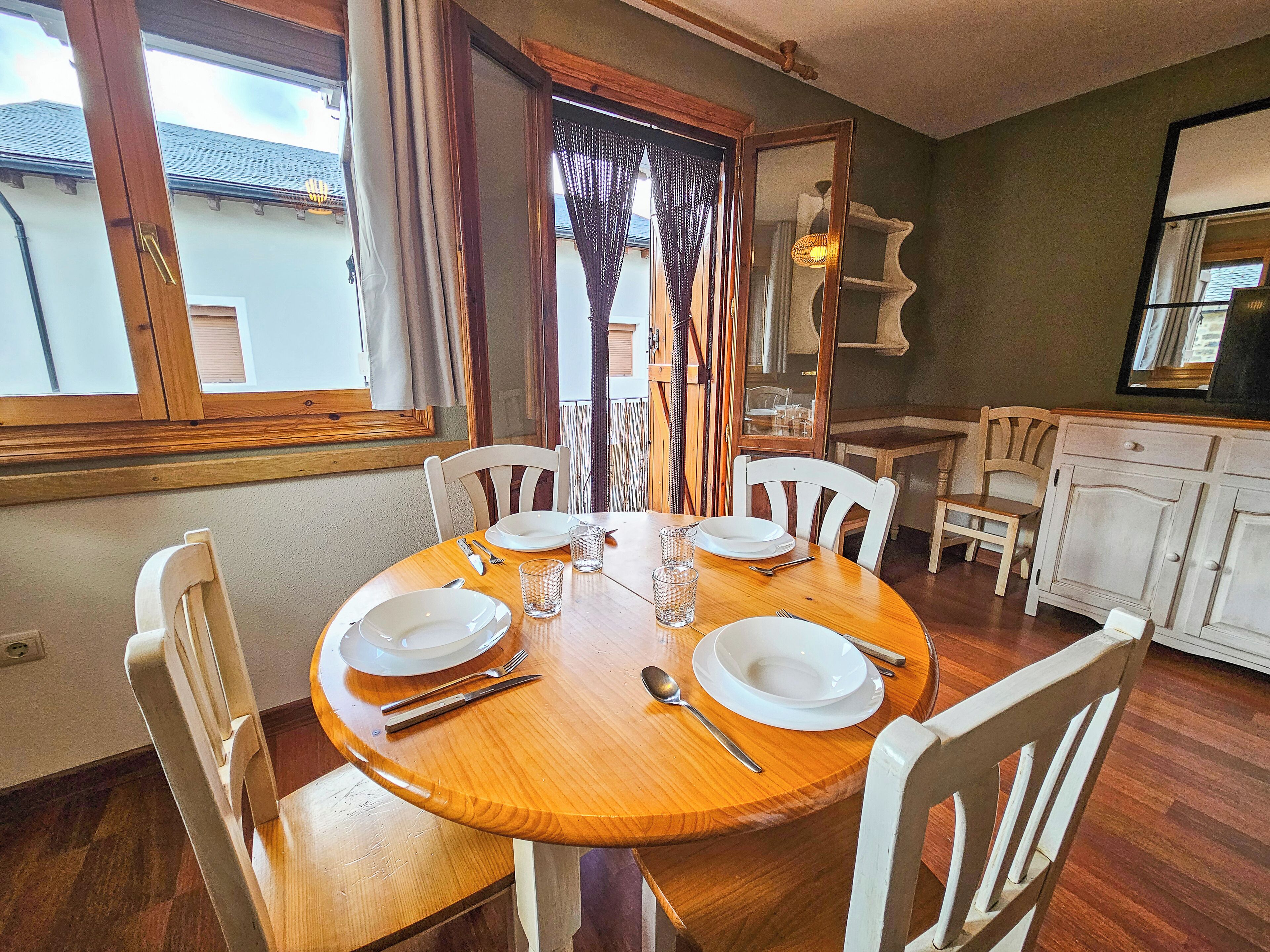 A dining area with a wooden table set for four, surrounded by white chairs.