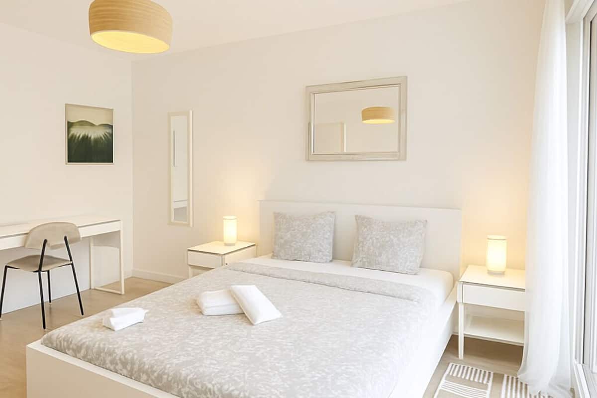 Un dormitorio moderno con una cama grande, mesitas de noche, un escritorio y una silla.