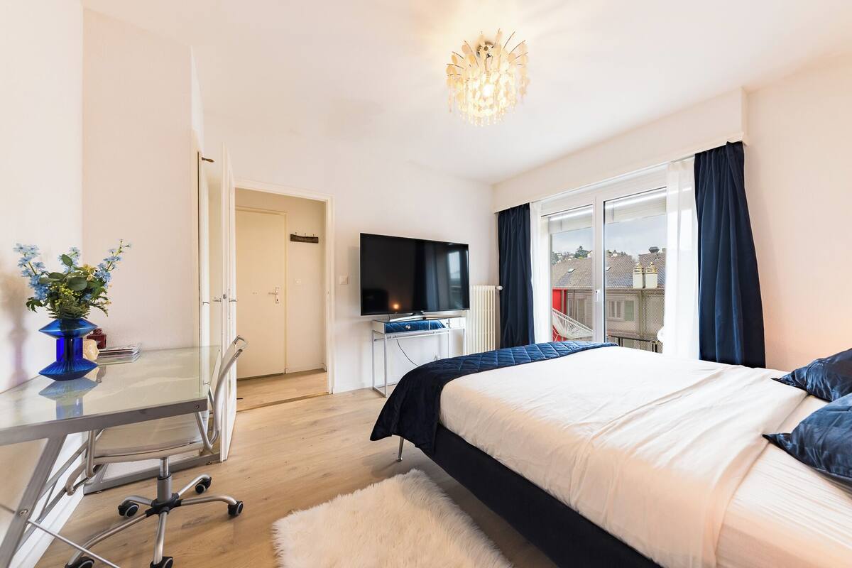 Una habitación de hotel moderna con una cama grande, un televisor de pantalla plana, un escritorio de cristal y vistas a la ciudad por la ventana.