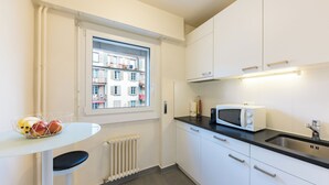 Une cuisine moderne avec des meubles blancs, un plan de travail noir, un four à micro-ondes et une fenêtre donnant sur un quartier résidentiel.