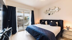 Une chambre moderne avec un grand lit, une porte vitrée donnant sur un balcon et une vue sur la ville.