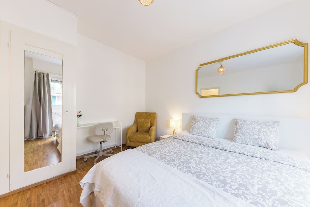 Un dormitorio con una cama grande, una silla, un escritorio y un espejo.