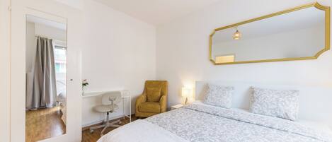 A bedroom with a large bed, a chair, a desk, and a mirror.