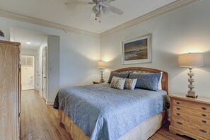 Ein Schlafzimmer mit einem Bett, zwei Nachttischen mit Lampen, einer Holzkommode, einem Deckenventilator und einem Bild an der Wand.
