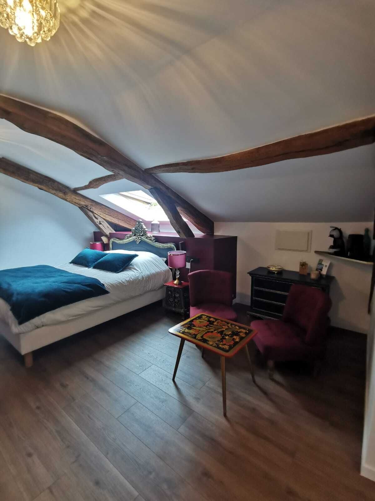 A bedroom with a bed, a small table, a chair, a desk, and a shelf.