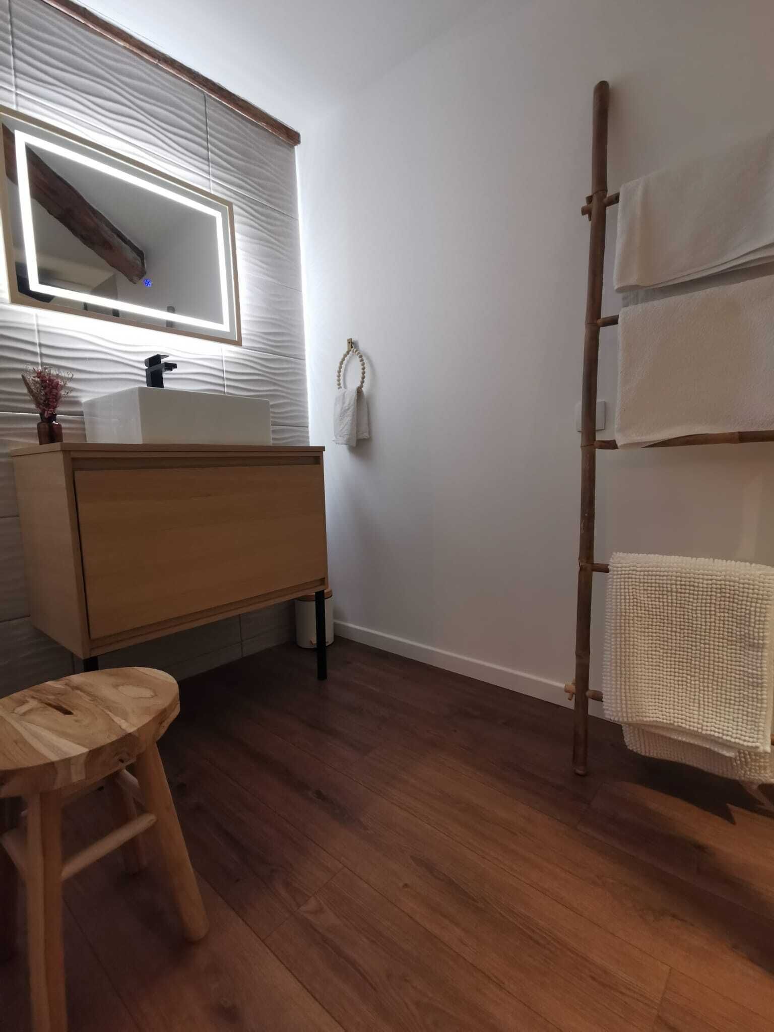 A bathroom with a wooden vanity, a mirror, a towel rack, and a wooden stool.