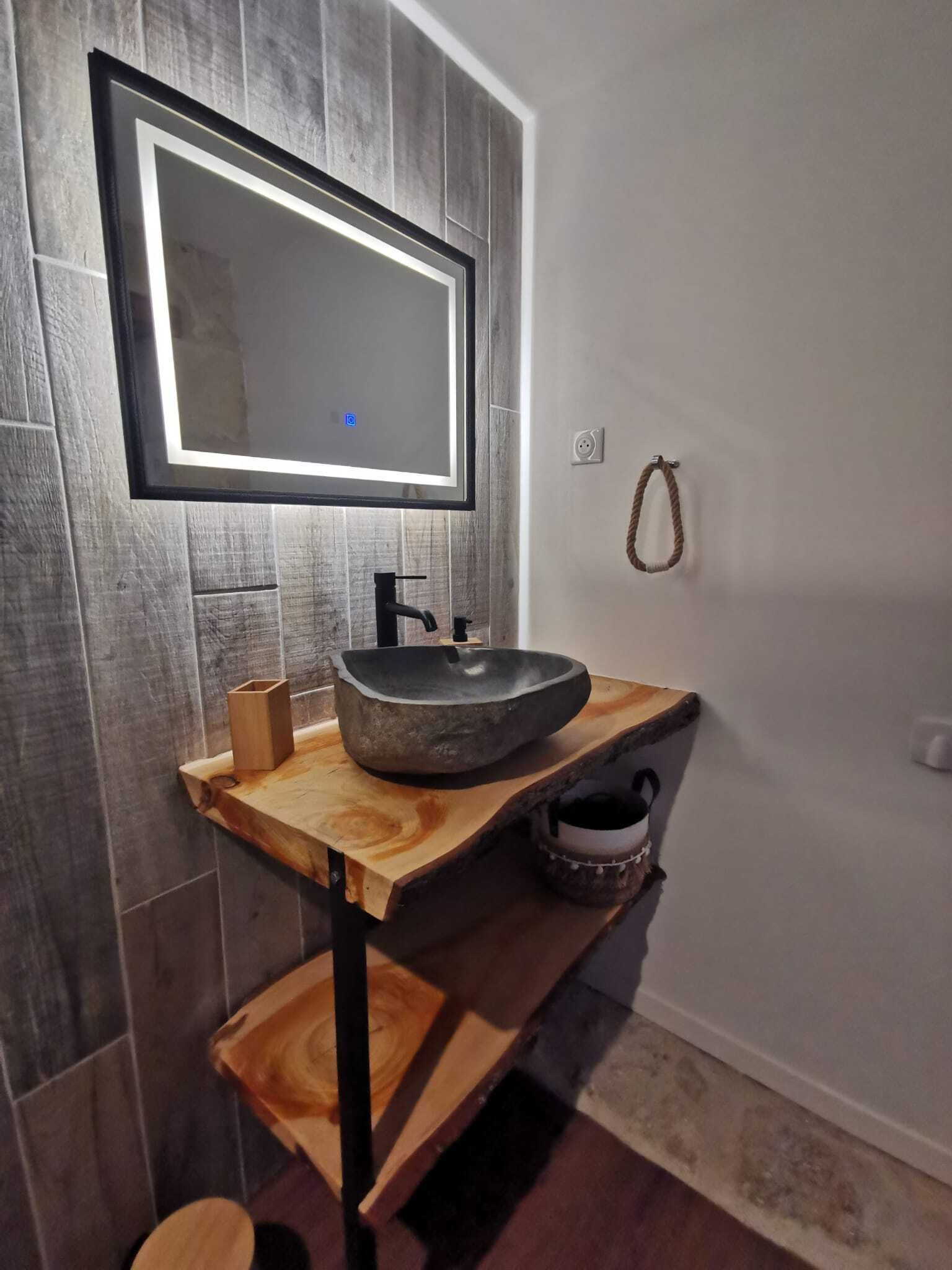A bathroom with a stone sink, wooden vanity, and a mirror with LED lighting.