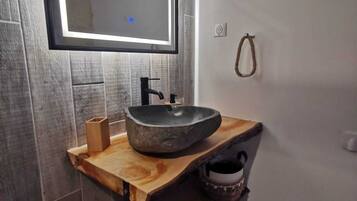 A bathroom with a stone sink, wooden vanity, and a mirror with LED lighting.