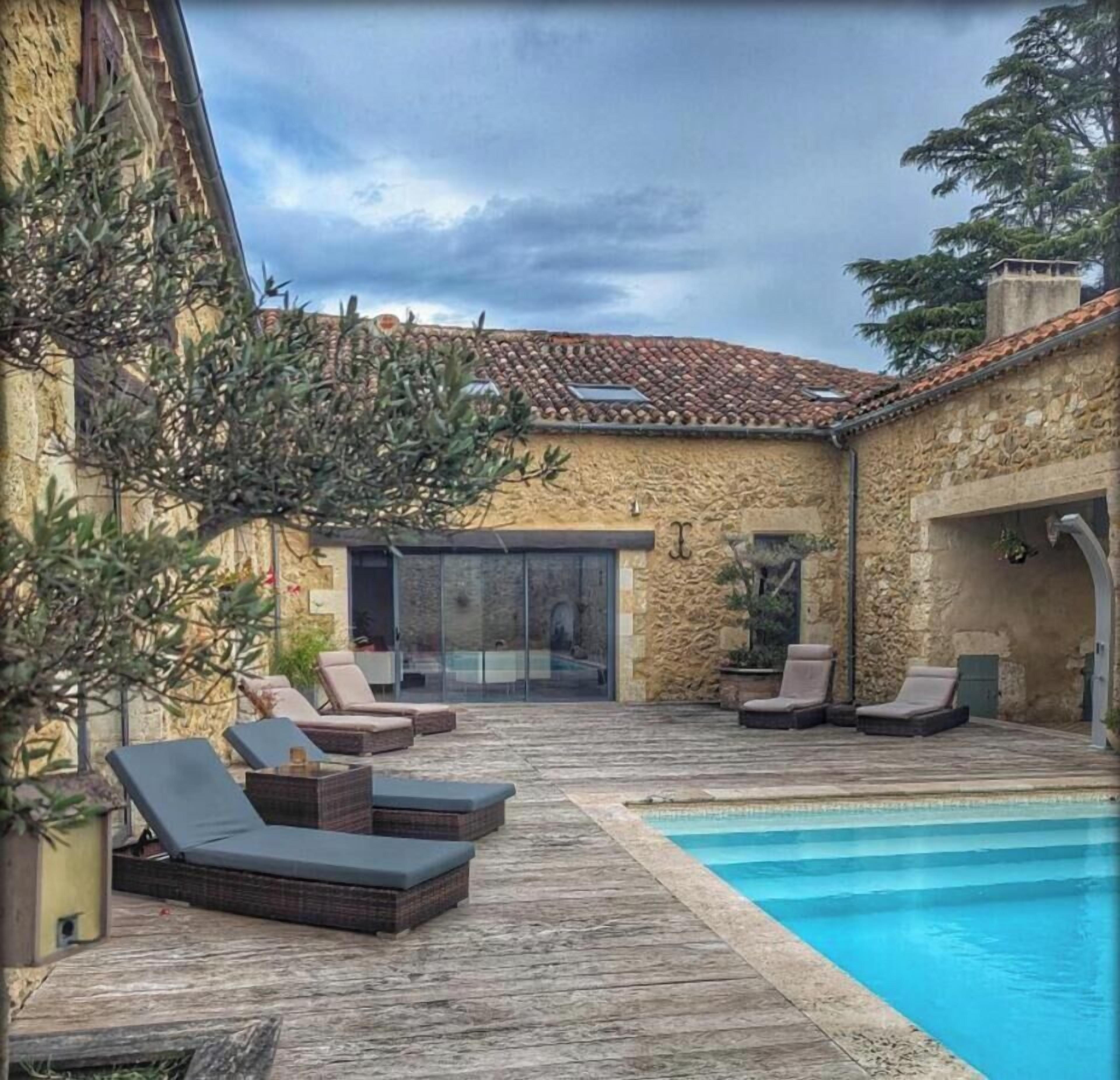 Zona junto a la piscina con sillas de descanso, un edificio de piedra y una piscina azul cristalina.