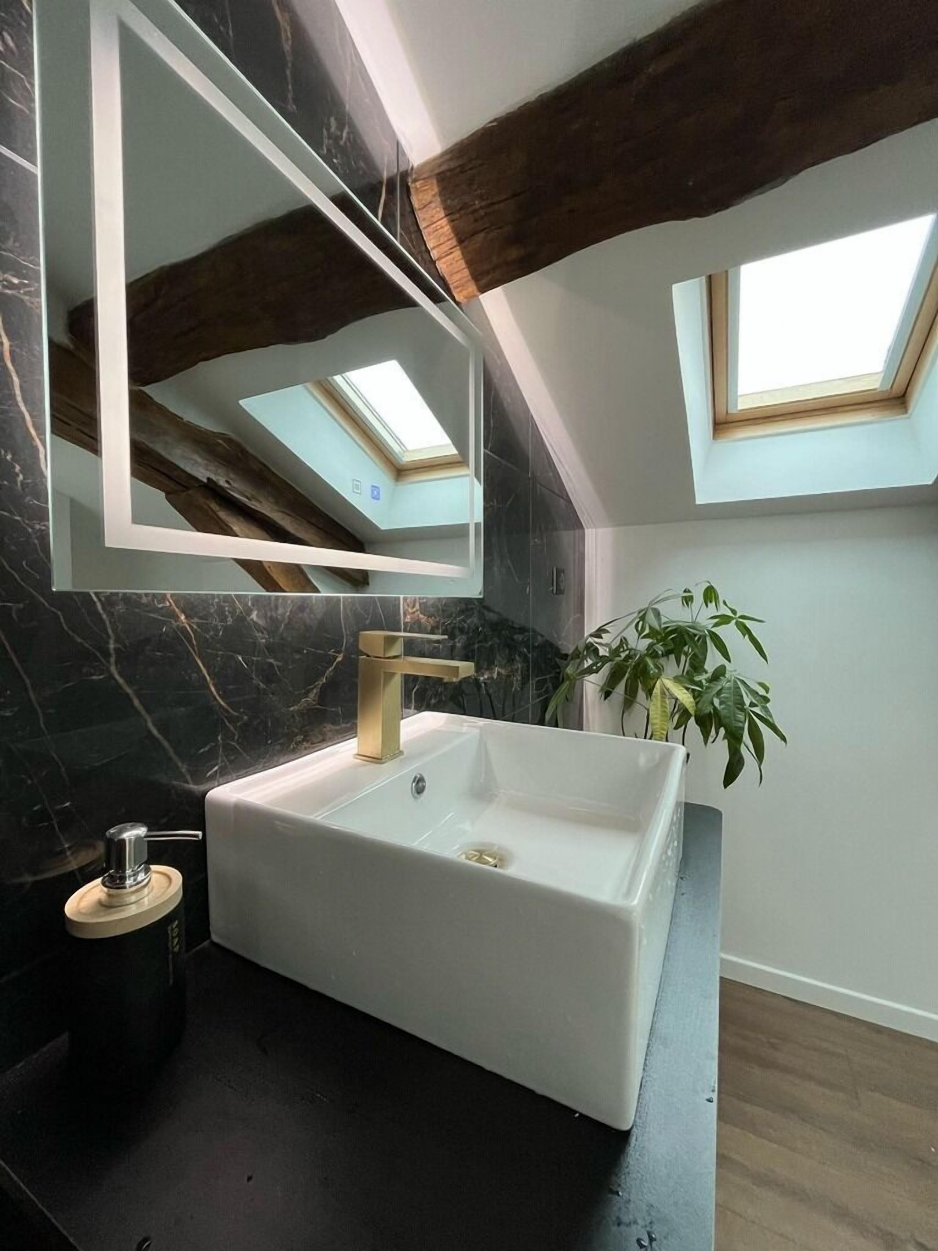 Un baño moderno con un lavamanos blanco, un espejo grande y un tragaluz.
