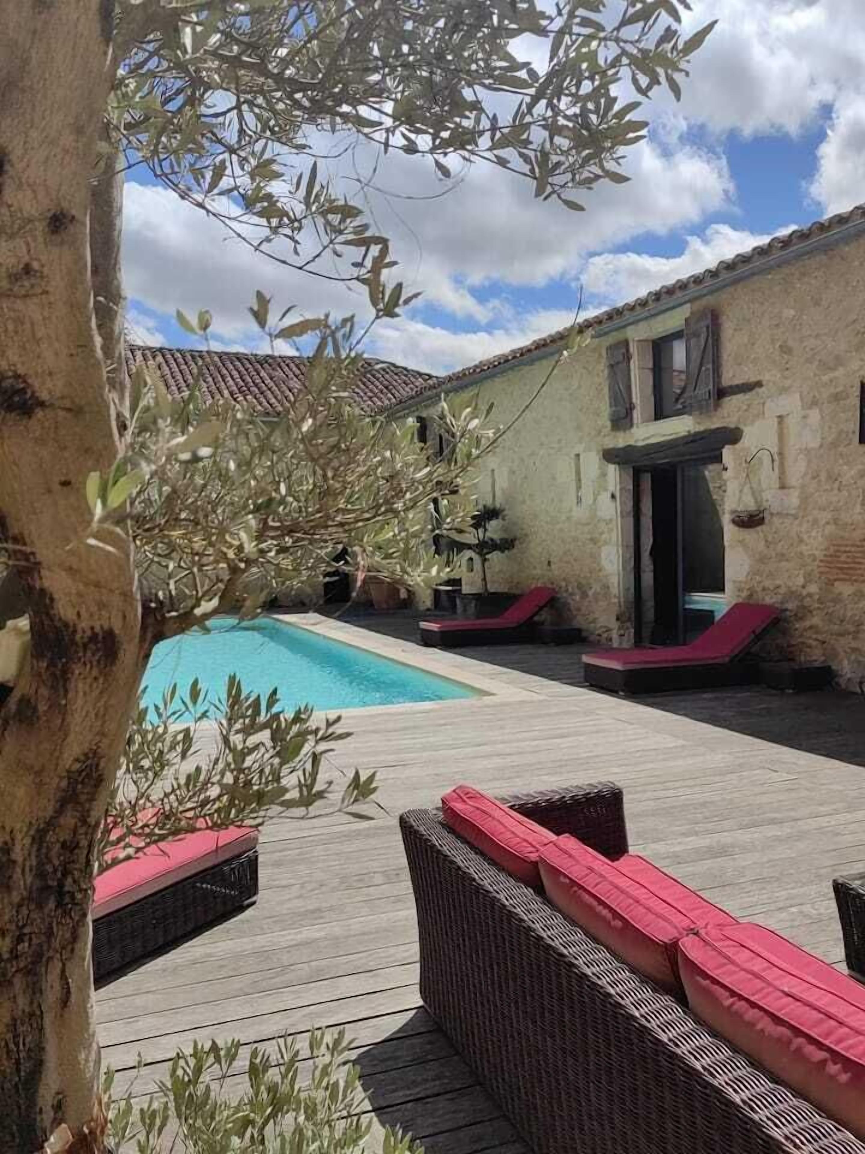 A pool area with a wooden deck, wicker furniture, and a stone building in the background.