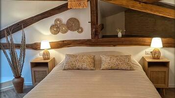A bedroom with a large bed, wooden beams, a hanging light fixture, and two bedside tables with lamps.