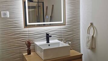 Un baño con un lavamanos rectangular, un espejo y un perchero para toallas.