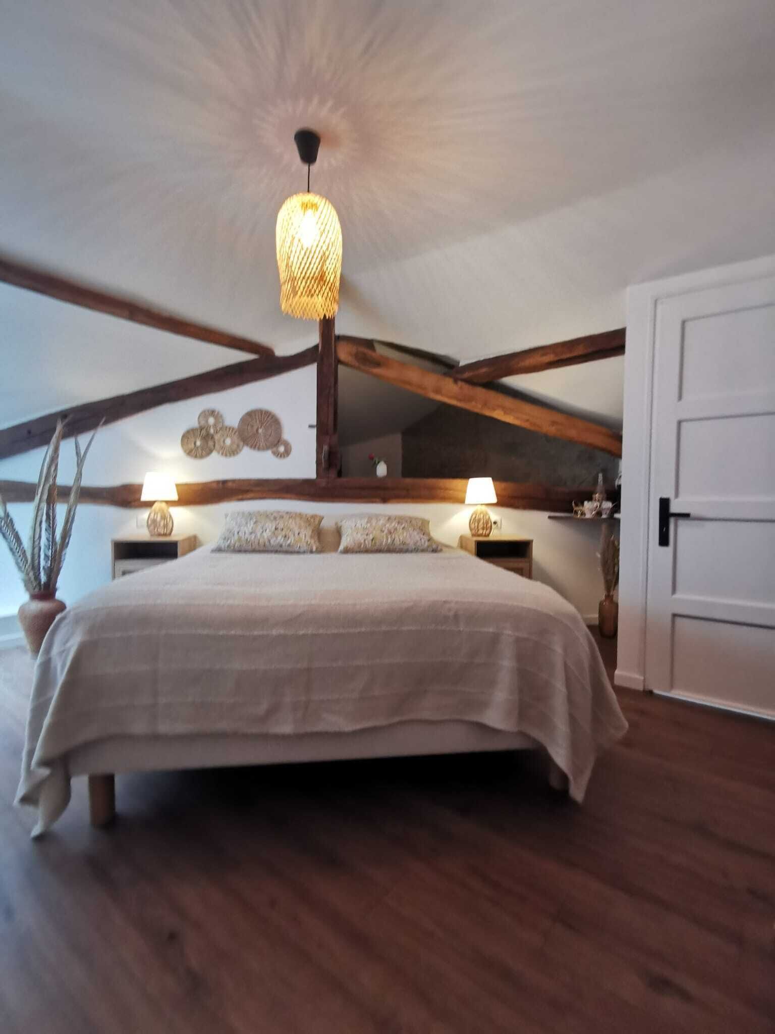 Un dormitorio con una cama grande, vigas de madera, una lámpara colgante y una puerta blanca.