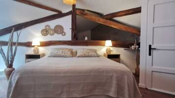 Un dormitorio con una cama grande, vigas de madera, una lámpara colgante y una puerta blanca.