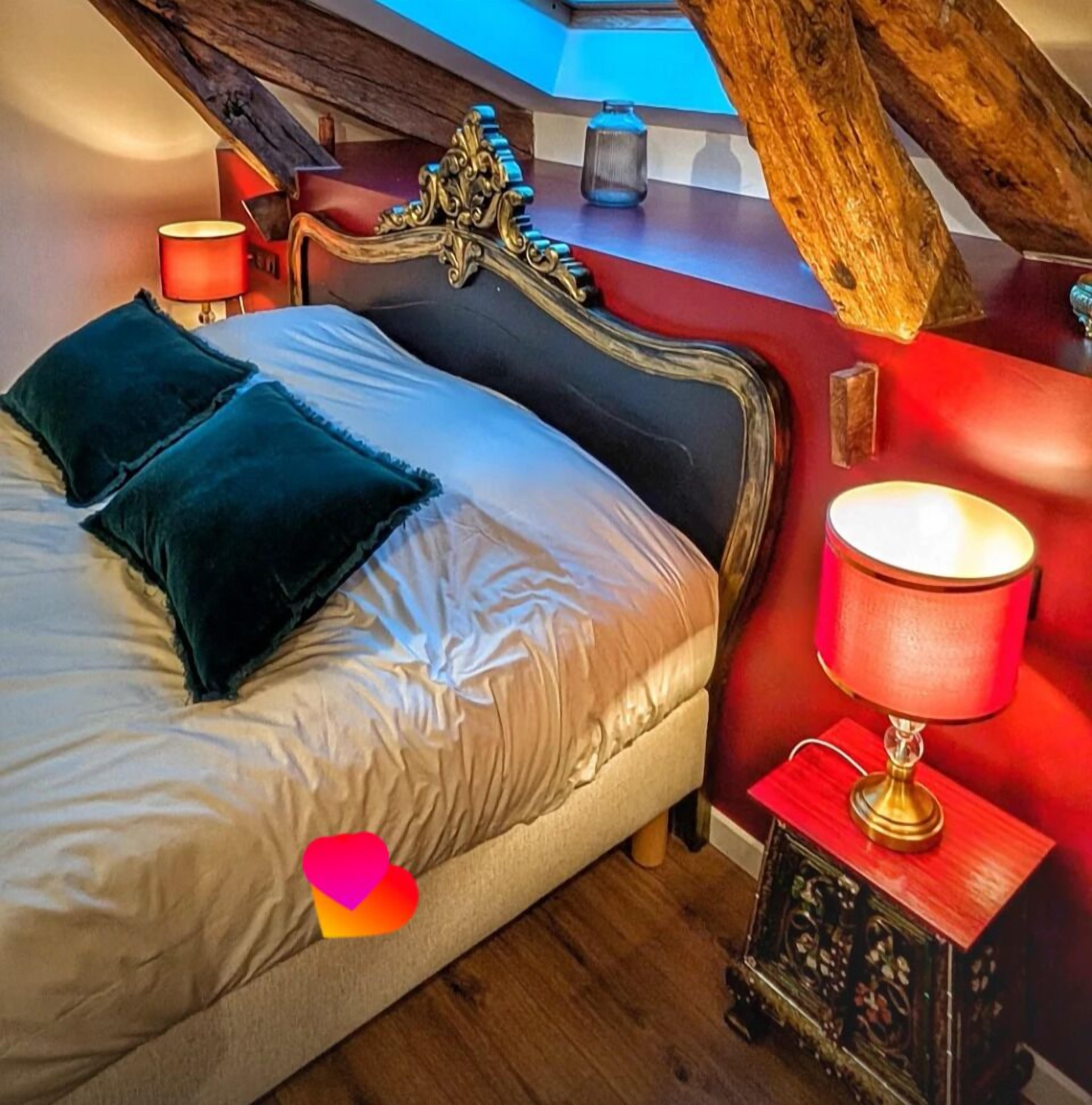 Une chambre à coucher avec un lit, des oreillers, une table de chevet avec une lampe et une structure en poutres apparentes.