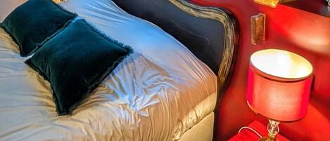 Un dormitorio con cama, almohadas, una mesita de noche con lámpara y estructura de vigas de madera.