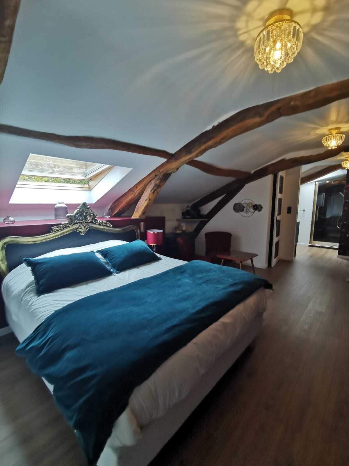 Un dormitorio con una cama grande, tragaluz, vigas de madera y una araña.