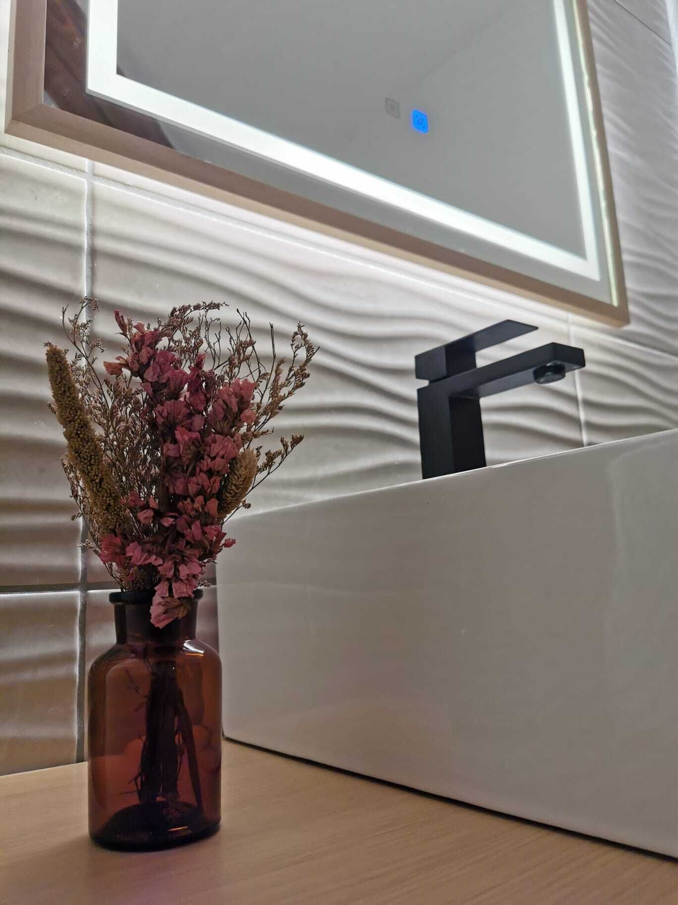 Une salle de bain dotée d’un lavabo moderne et d’un vase rempli de fleurs séchées posé sur le comptoir.