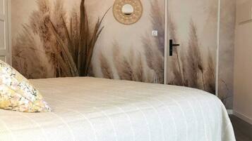 A bedroom with a bed, a door, a wall-mounted mirror, and a hanging light fixture.