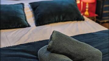Een netjes opgemaakt bed met donkere dekbedden en twee kussens, een lamp op een nachtkastje, en een rode muur op de achtergrond.