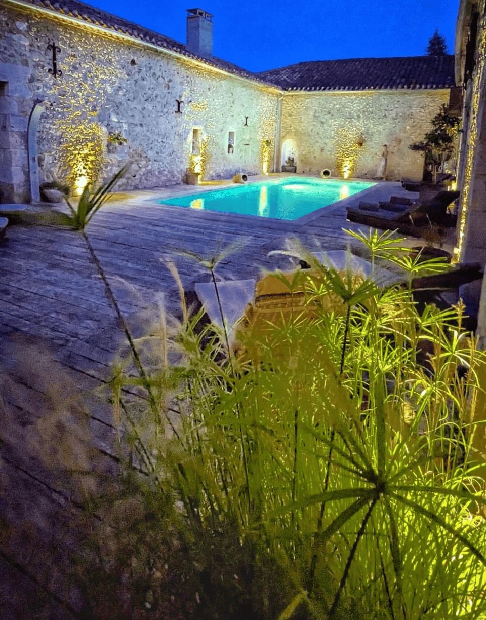 Un patio de piedra con piscina, muros de piedra y mobiliario exterior.